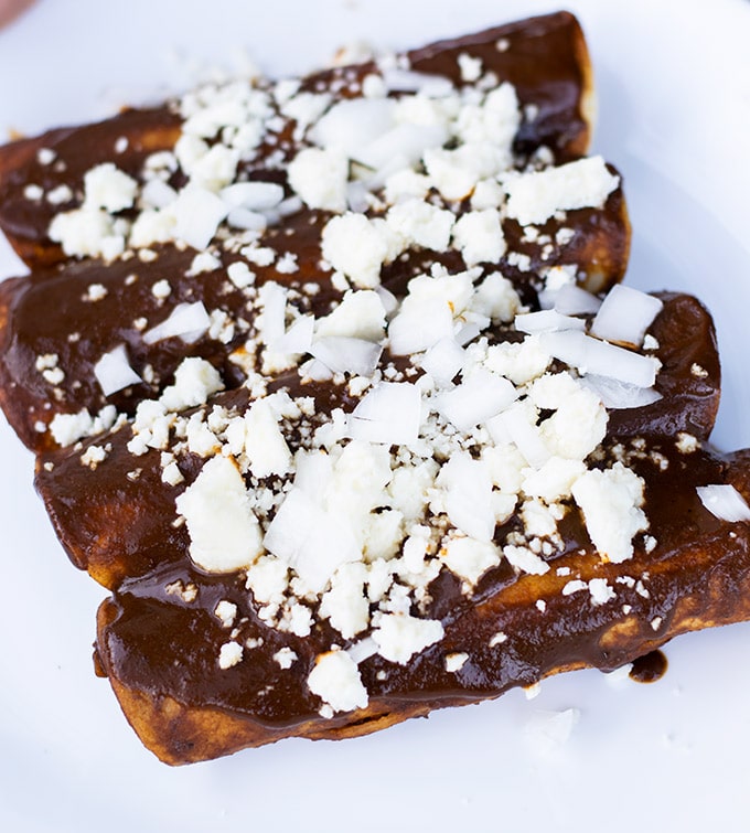 enmoladas on a plate garnished with diced onion and crumbled queso fresco