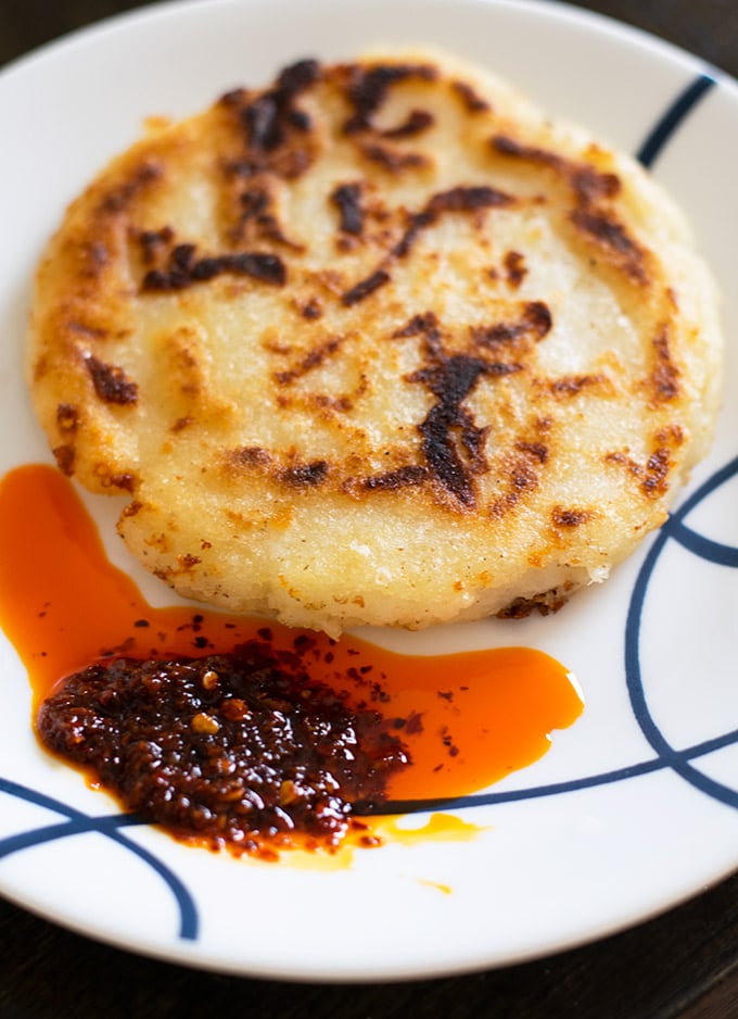 arepa con queso on a plate with salsa macha.