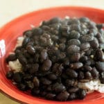 black beans served over white rice on a red plate