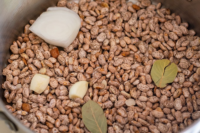 dried beans, piece of onion, two garlic cloves and two bay leaves in a pot