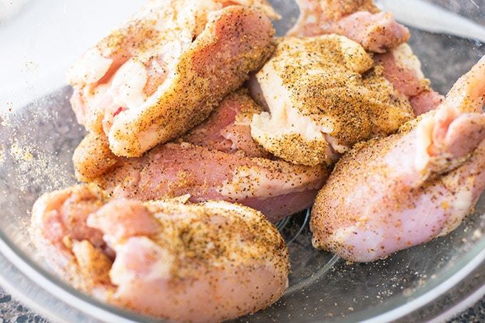 raw chicken thighs in a bowl with seasoning