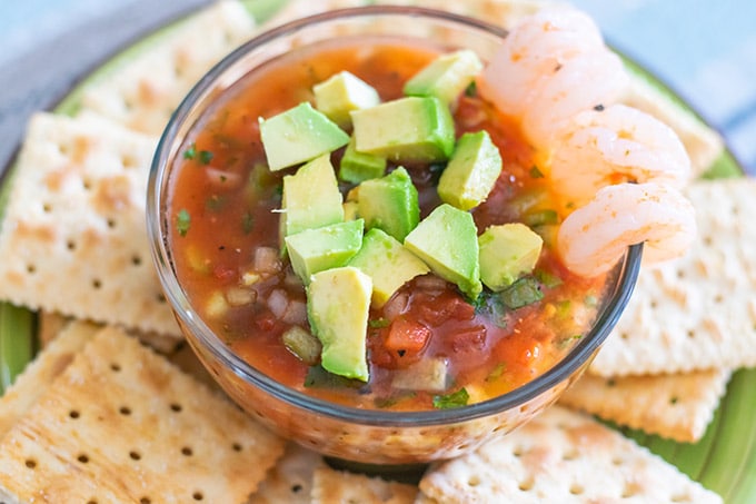 A bowl of coctel de camaron on a green plate with saltine crackers.