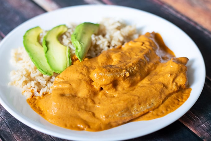 creamy chipotle chicken on a white plate with rice and sliced avocado