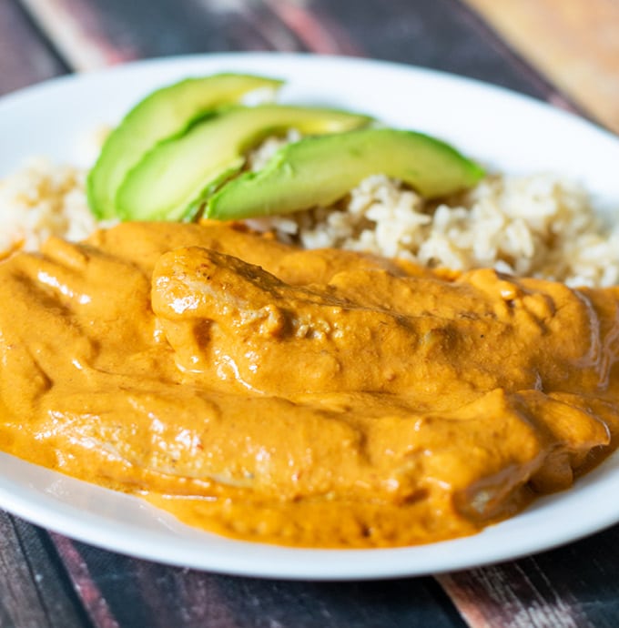 creamy chipotle chicken on a white plate with white rice and sliced avocado