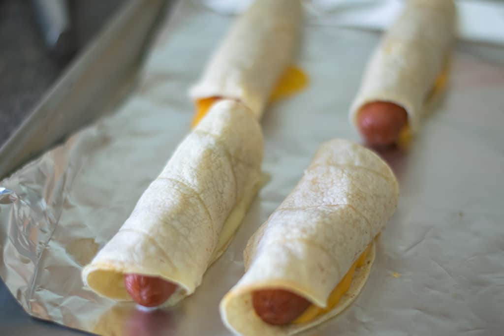baked tortilla wrapped hot dogs on a baking sheet