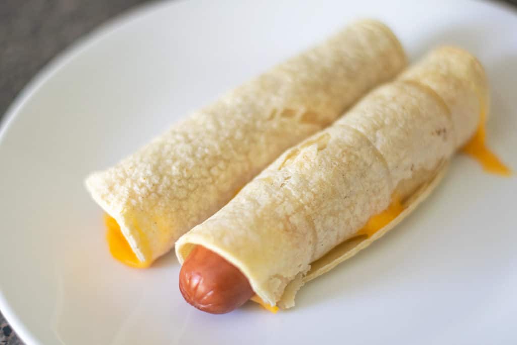 baked tortilla wrapped hot dogs on a white plate