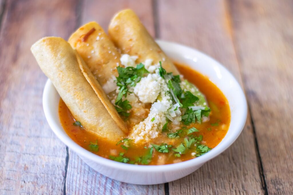 chicken taquitos served in a white bowl with consome