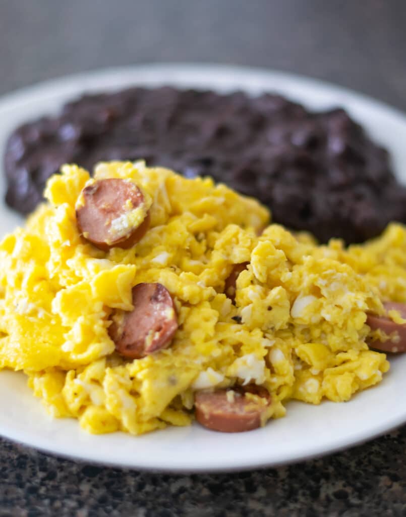 huevos con salchicha and refried black beans on a white plate