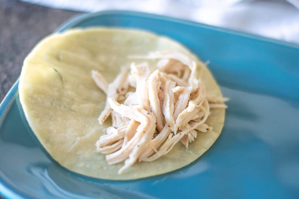 A tortilla on a blue plate with shredded chicken.