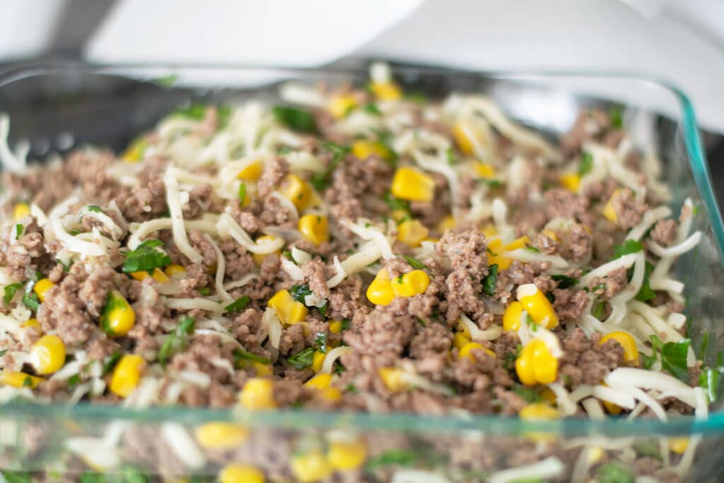 ground beef, corn and shredded cheese in a glass bowl.