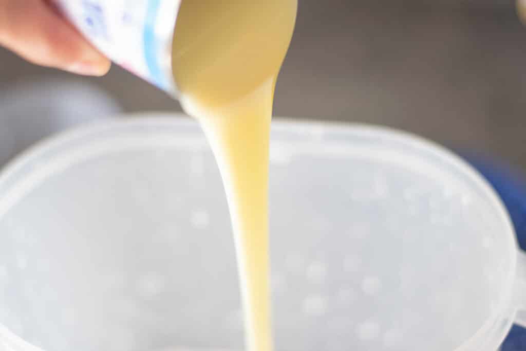 Pouring sweetened condensed milk into a pitcher.