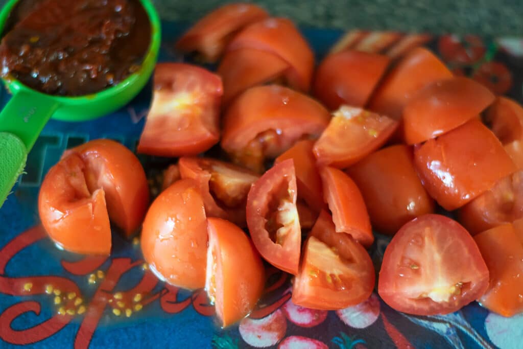 chopped roma tomatoes on a cutting board along with half a cup of chipotle peppers in adobo.