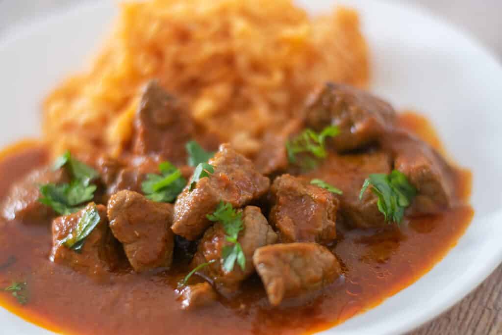Beef stew and rice on a white plate.
