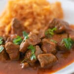 Beef stew with tomato sauce and rice on a white plate.