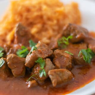 Beef stew with tomato sauce and rice on a white plate.