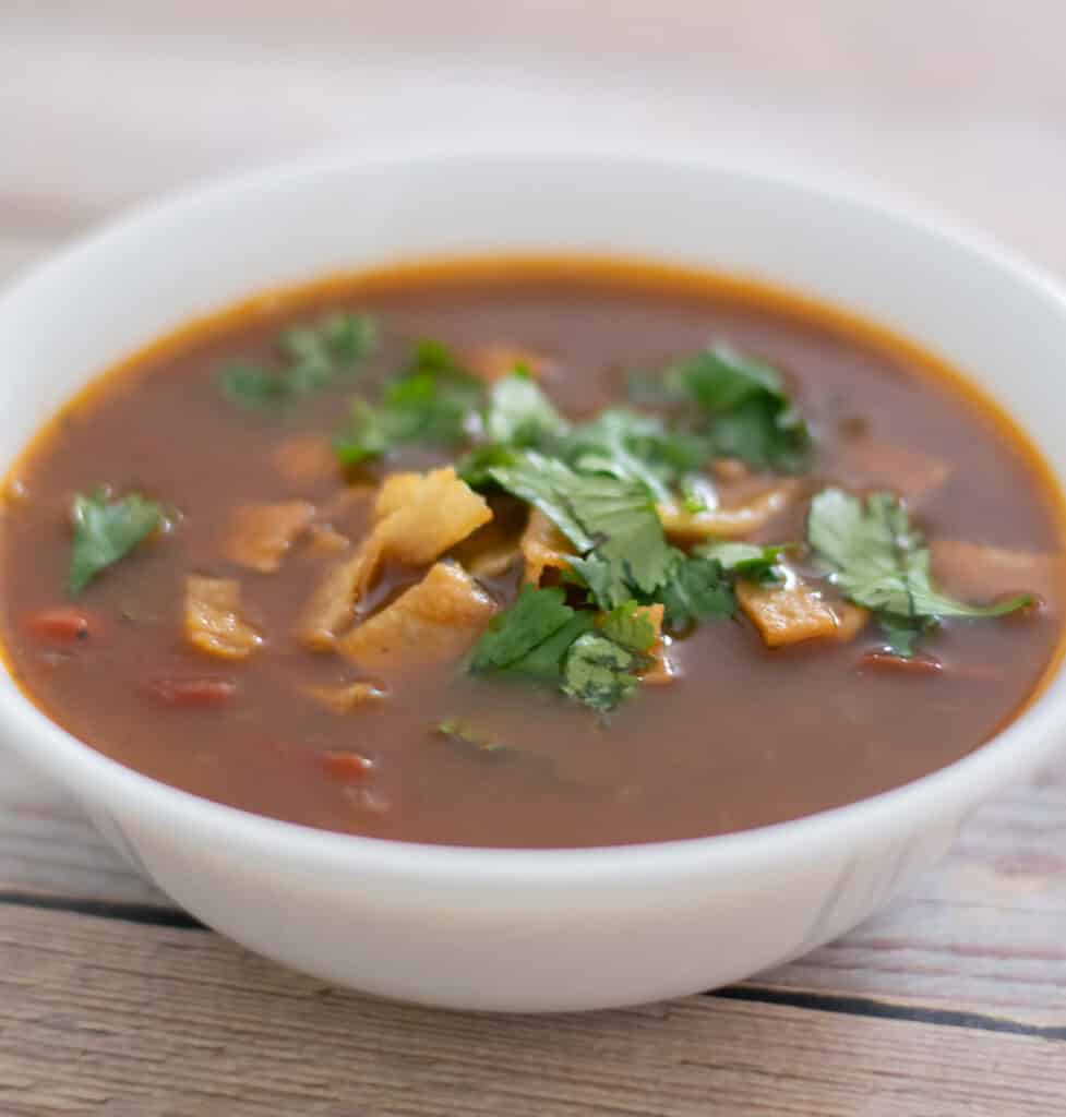 black bean tortilla soup garnished with chopped cilantro in a white bowl.