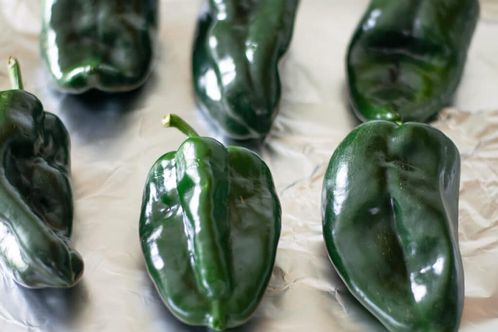 Six poblano peppers on a foil lined baking sheet.