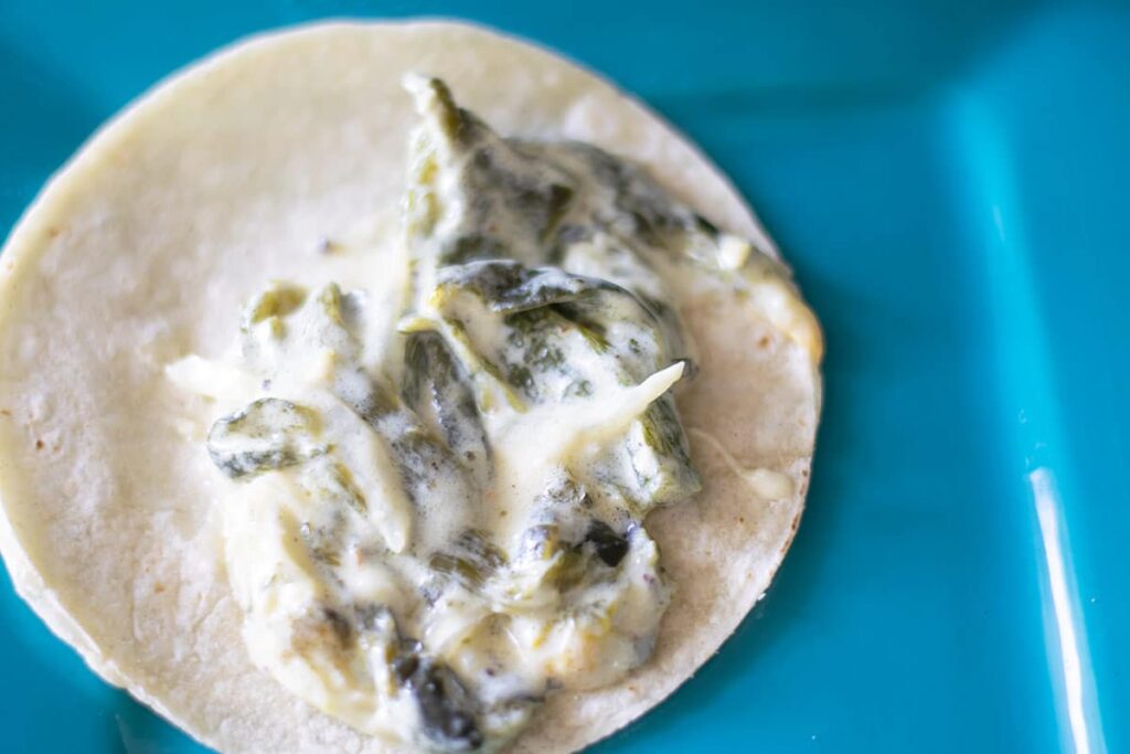 A tortilla with rajas con crema on a blue plate.