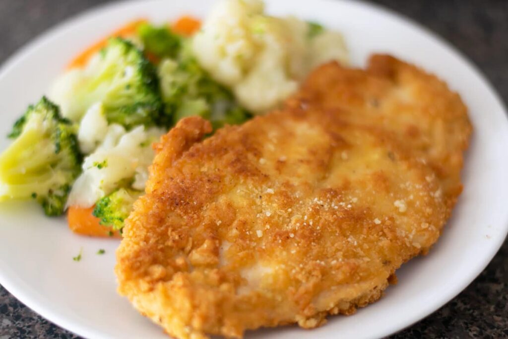Breaded chicken with steamed veggies on a white plate.