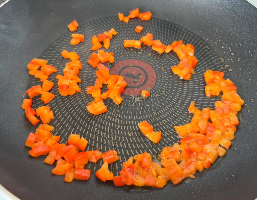 Diced red bell pepper cooking in a skillet.