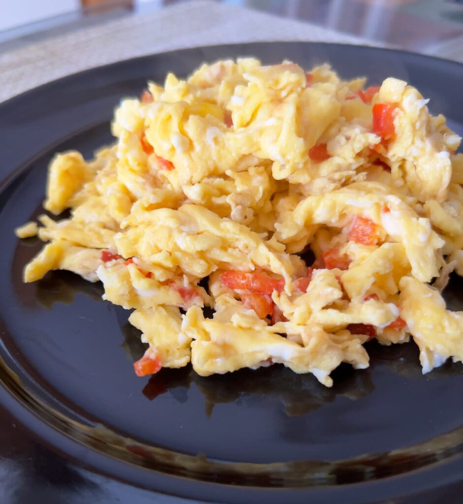 Scrambled eggs with red bell pepper on a black plate.