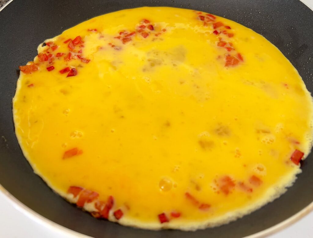 Making scrambled eggs with red bell pepper in a skillet.