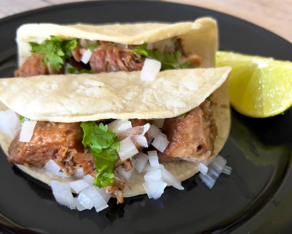 Dutch oven carnitas tacos on a black plate.