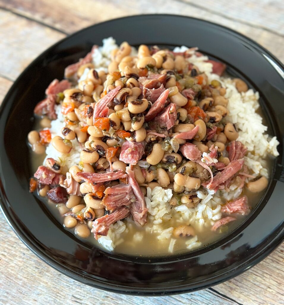 Black eyed peas with ham hock over rice on a black plate.