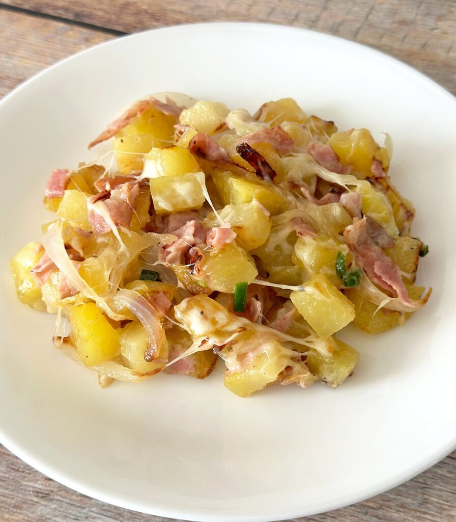 Cheesy Mexican potatoes with ham on a white plate.
