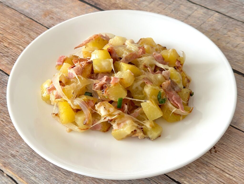 Mexican style potatoes with ham and cheese on a white plate.