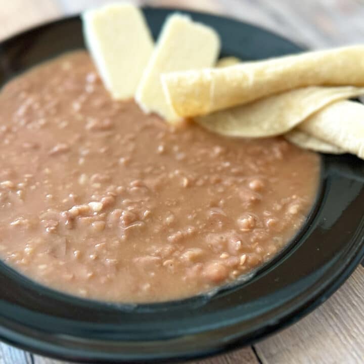 Mashed beans, queso fresco and tortillas on a black plate.