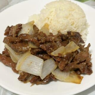 Beef and onion stir fry with jasmine rice on a white plate.