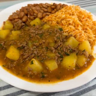 Picadillo con papas on a plate with rice and beans.