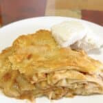 A slice of homemade apple pie with vanilla ice cream on a white plate.