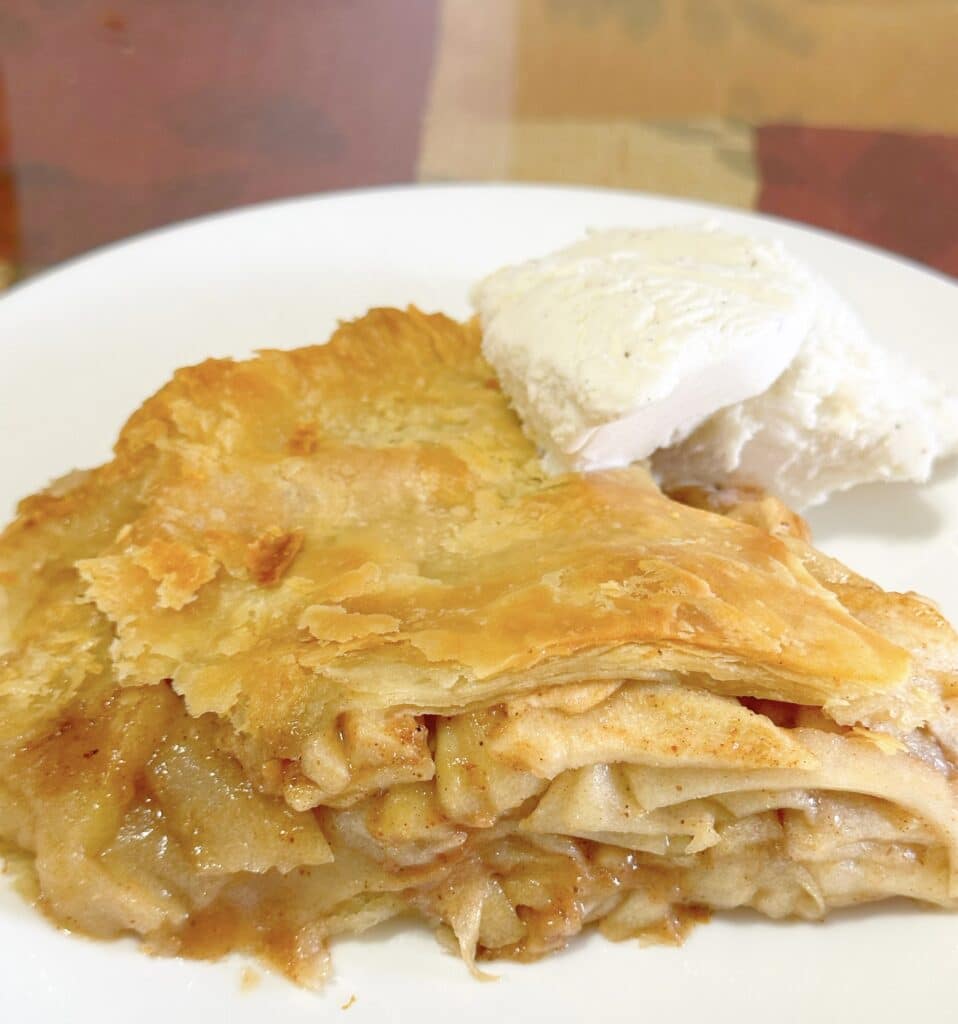A slice of homemade apple pie with vanilla ice cream on a white plate.