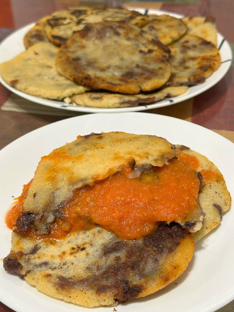 Black bean and cheese pupusas with salsa on a white plate.