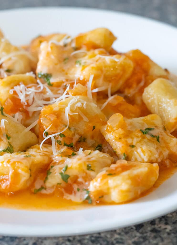 Gnocchi in tomato sauce on a white plate garnished with grated parmesan and parsley.