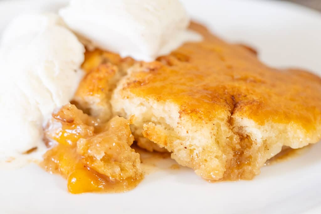 Slice of homemade peach cobbler with canned peaches served with vanilla ice cream.