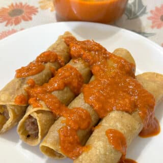 Beef and bean taquitos topped with salsa on a white plate.