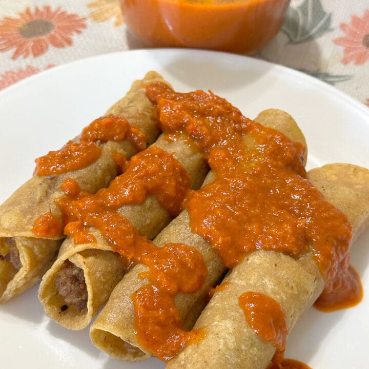 Beef and bean taquitos topped with salsa on a white plate.