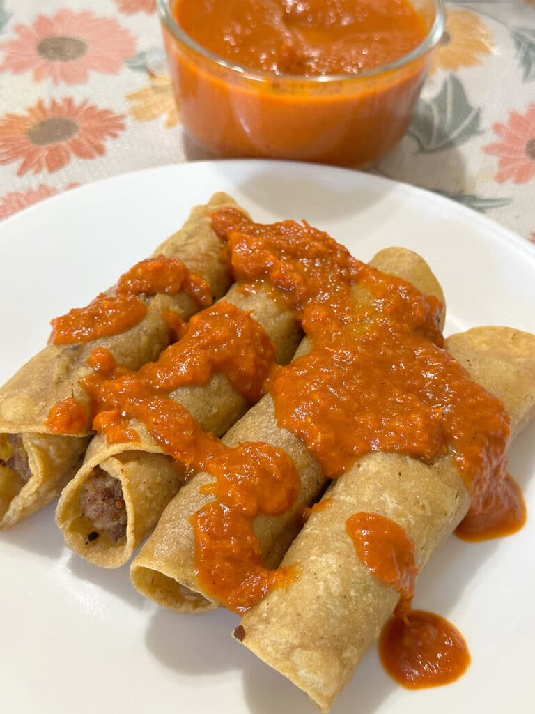 Beef and bean taquitos topped with salsa on a white plate.