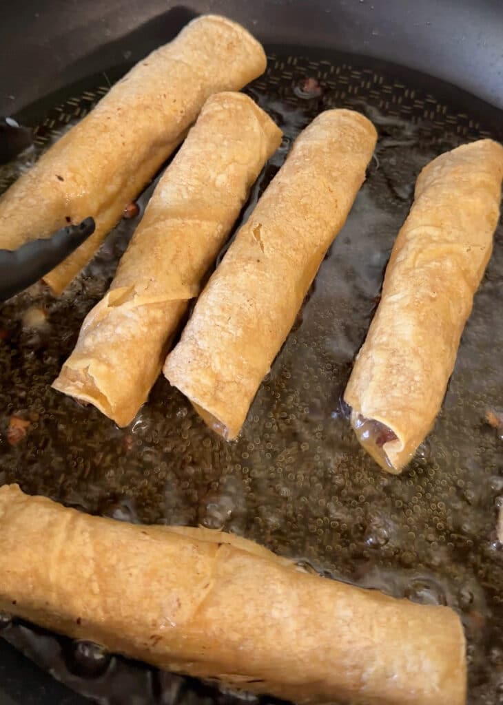 Frying beef and bean taquitos in a skillet.