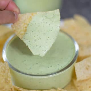 Creamy jalapeño dip in a bowl on a plate with chips.