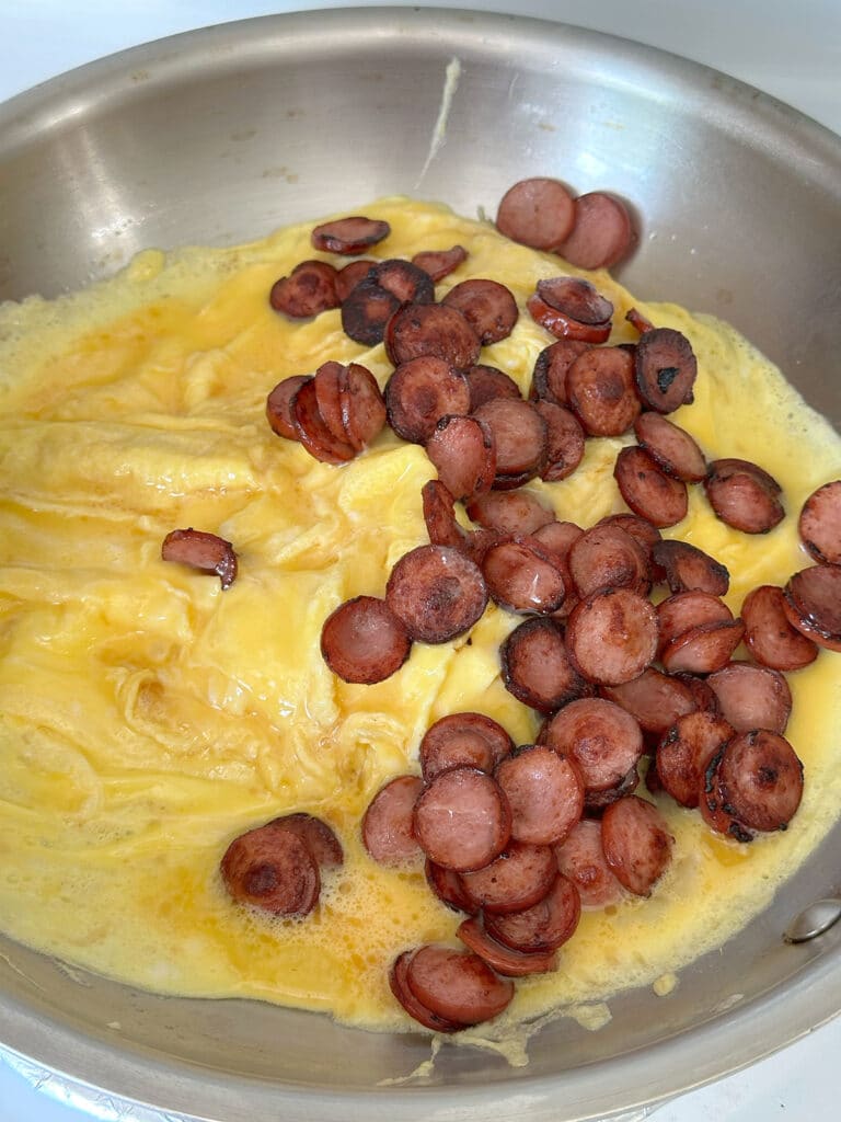 Cooking scrambled eggs and hot dogs in a pan.